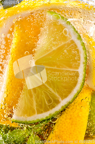 Image of In a clear glass mint leaf, slices of lime and lemon with bubbles. Macro photo of summer drink mojito