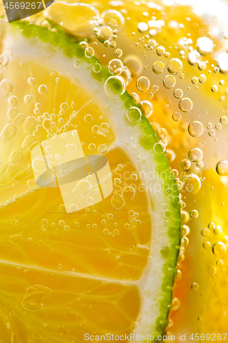 Image of Juicy slices of ripe lemon and lime with bubbles in a glass of water. Macro photo of refreshing lemonade