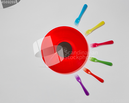 Image of Colorful plastic forks around red vinyl record on a light gray background.