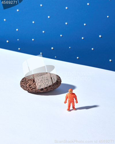 Image of Plastic toy of spaceman and moonstone on a light surface against blue star sky background.