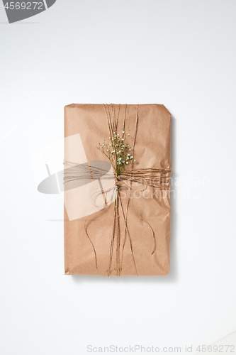 Image of A gift wrapped in craft paper and decorated with flowers on a light background with copy space. Flat lay