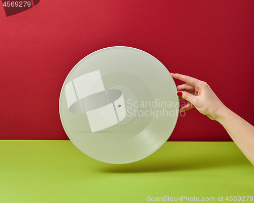 Image of Woman\'s hand is holding a white vinyl audio record on a duotone red green background with a copy space.