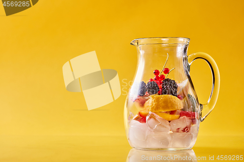 Image of Glass jug with citrus, berries and ice on a yellow background.