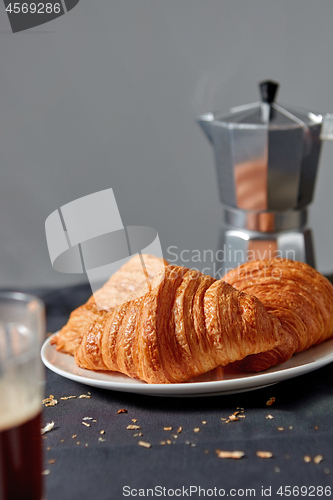Image of Coffee maker with homemade croissant on a gray background.