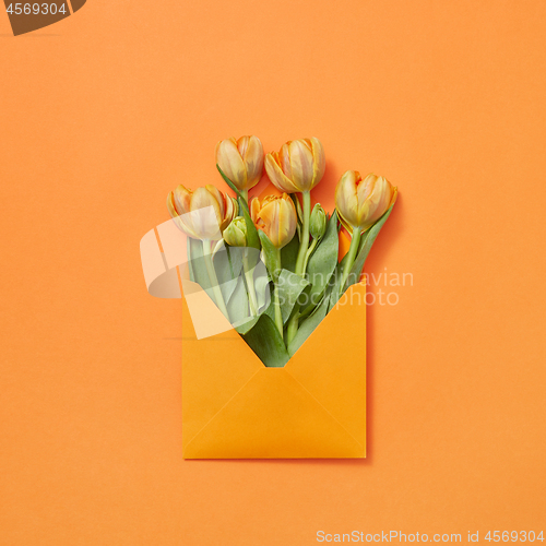 Image of Post card with bouquet of tulips in craft envelope on an orange background.