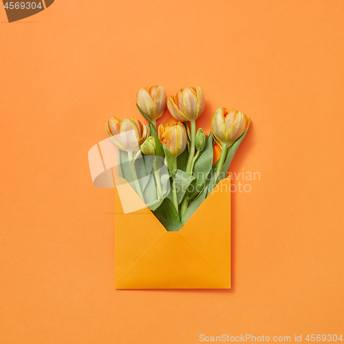 Image of Post card with bouquet of tulips in craft envelope on an orange background.