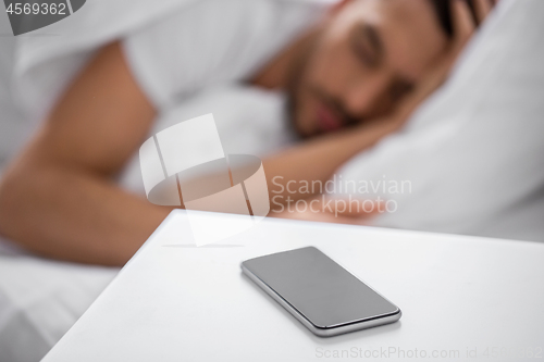 Image of smartphone on bedside table near sleeping man