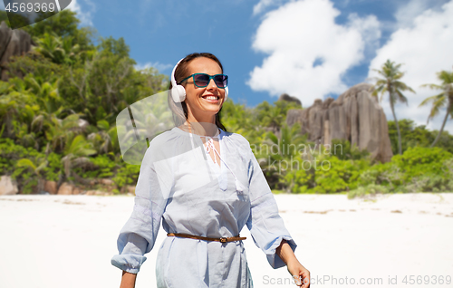 Image of woman with headphones walking along summer beach