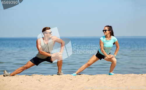 Image of smiling couple stretching legs on beach