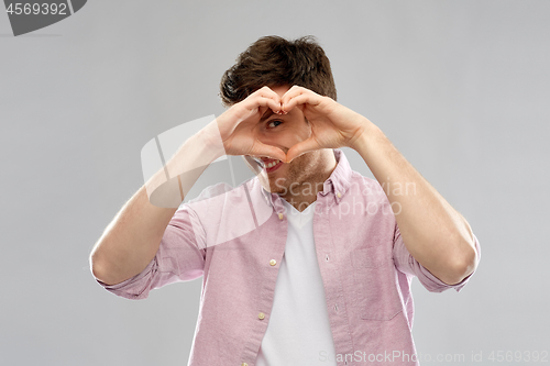 Image of man making hand heart gesture over grey background