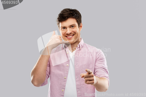 Image of smiling young man showing phone call gesture