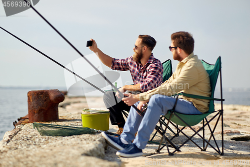 Image of friends fishing and taking selfie by smartphone