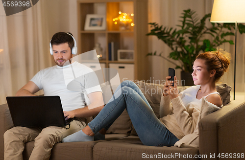 Image of couple with laptop and smartphone resting at home