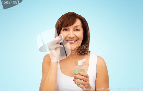 Image of senior woman cleaning face by lotion on cotton pad