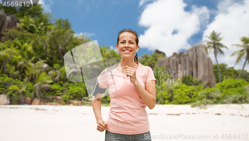 Image of woman with earphones and armband running on beach