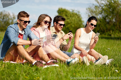 Image of smiling friends with smartphones sitting on grass