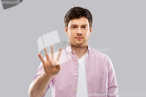 Image of young man showing four fingers over grey