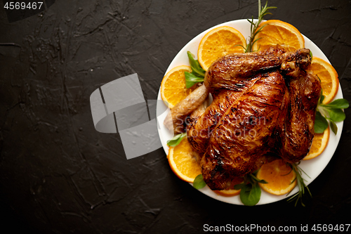 Image of Roasted whole chicken or turkey served in white ceramic plate with oranges