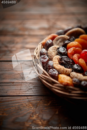 Image of Mix of dried fruits in a small wicker basket on wooden table