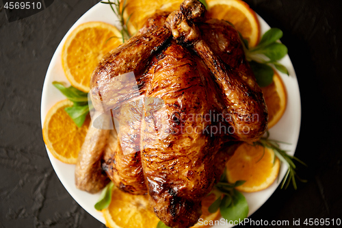 Image of Roasted whole chicken or turkey served in white ceramic plate with oranges