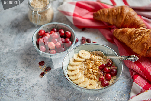 Image of Ceramic bowl of oatmeal porridge with banana, fresh cranberries and walnuts