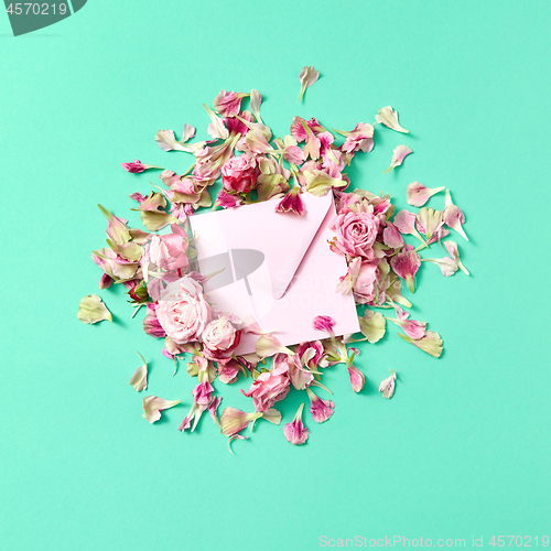 Image of Greetings post card with fresh roses and craft envelope on a turquoise background.