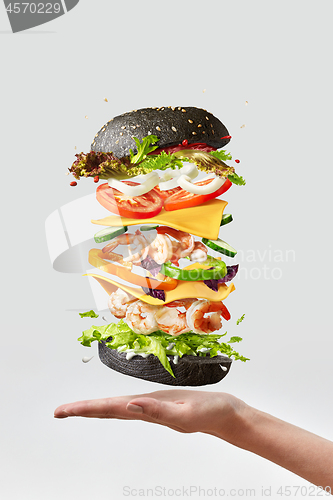 Image of Healthy homemade burger with fresh shrimp and vegetables above the hand on a light background.