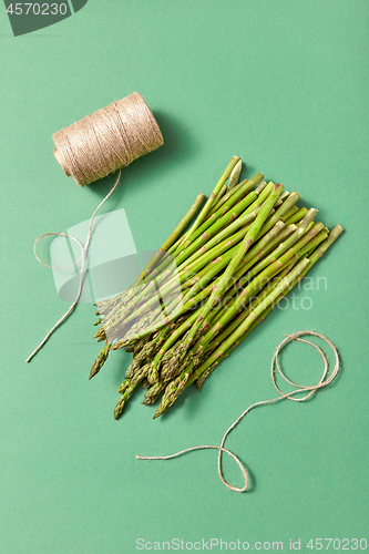 Image of Bunch of natural healthy asparagus and a coil of rope on a green background.
