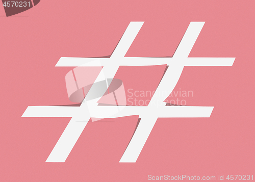 Image of White hashtag symbol cut from pastel pink paper as a background.
