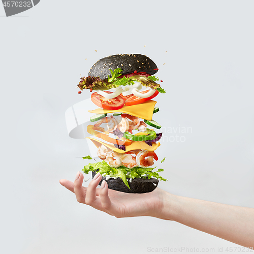 Image of Woman\'s hand holds healthy sandwich from fresh seafood and vegetables on a light background.