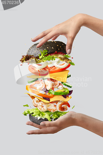 Image of Flying burger with fresh ingredients between woman\'s hands on a light background.