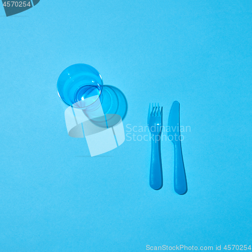 Image of Plastic glass, fork and knife with shadows on a blue table.