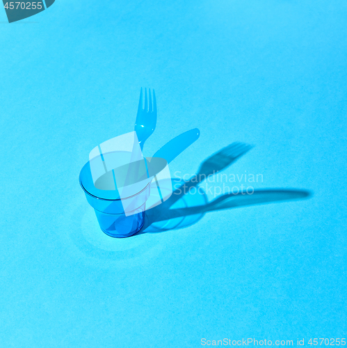 Image of Plastic transparent glass with fork and knife with shadows on surface.