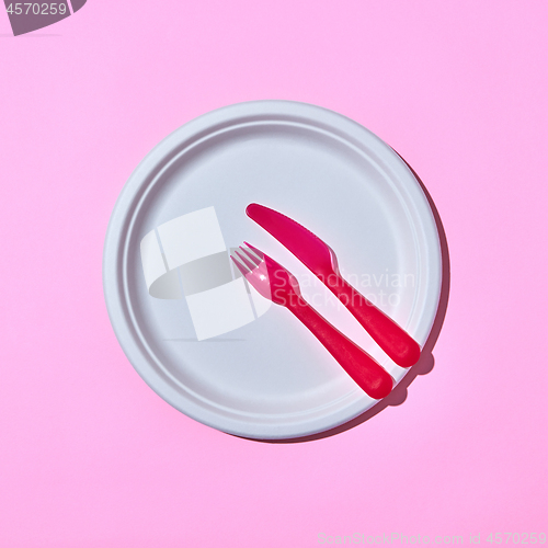 Image of Served place with disposable plastic utensils on pink.