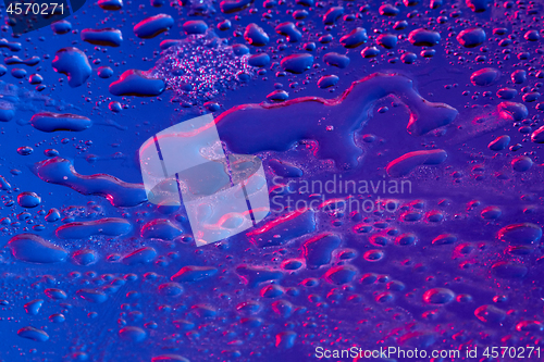 Image of Neon lighted water droplets on a blue surface.