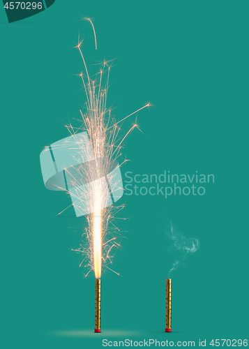 Image of Two fireworks burning and burnt on a turquoise background.