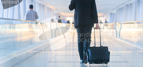 Image of Businessman walking and wheeling a trolley suitcase at the lobby, talking on a mobile phone. Business travel concept.