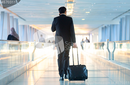 Image of Businessman walking and wheeling a trolley suitcase at the lobby, talking on a mobile phone. Business travel concept.