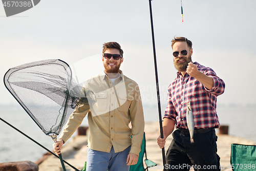 Image of friends with fishing rod, fish and tackle on pier