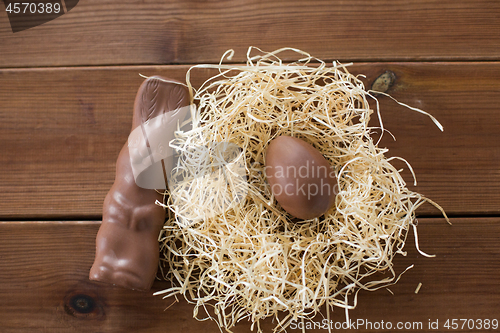 Image of chocolate bunny and egg in straw nest on wood