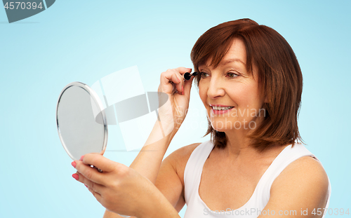 Image of smiling senior woman with mirror applying mascara