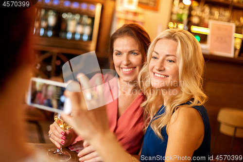 Image of woman picturing friends by smartphone at wine bar