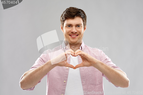 Image of man making hand heart gesture over gey background