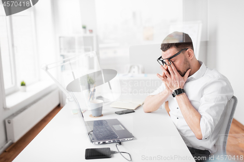 Image of tired businessman rubbing eyes at office