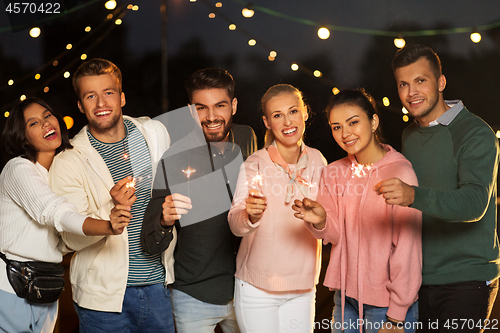 Image of happy friends with sparklers at rooftop party