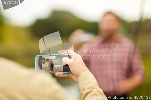 Image of friend photographing fisherman by smartphone