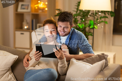 Image of happy couple using tablet pc at home in evening