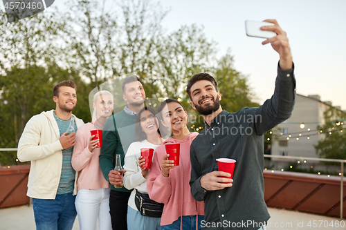 Image of friends with drinks taking selfie at rooftop party