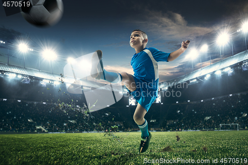 Image of Young boy with soccer ball doing flying kick at stadium