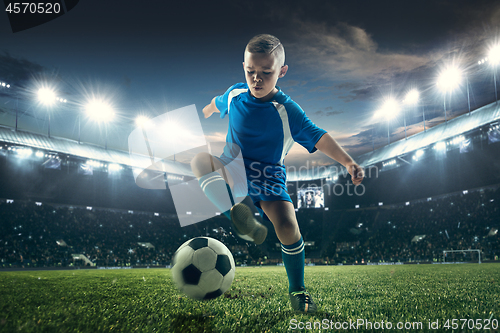 Image of Young boy with soccer ball doing flying kick at stadium